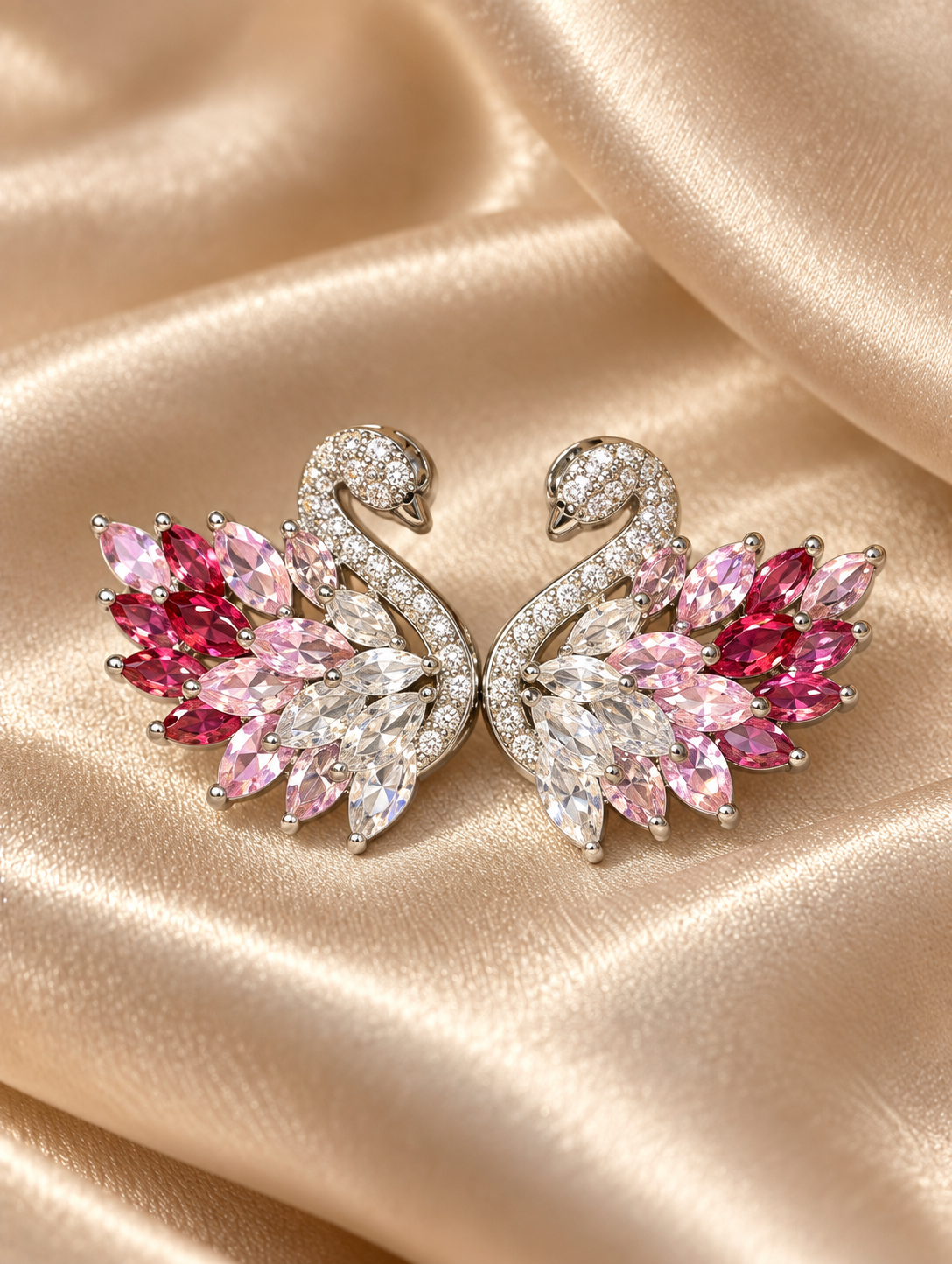 Nahaufnahme der Rosentraum Schwan-Ohrstecker auf hellem Satin: Zirkonia-besetzte Schwanenhälse und marquiseförmige Flügelsteine in Weiß, Rosa und Himbeer