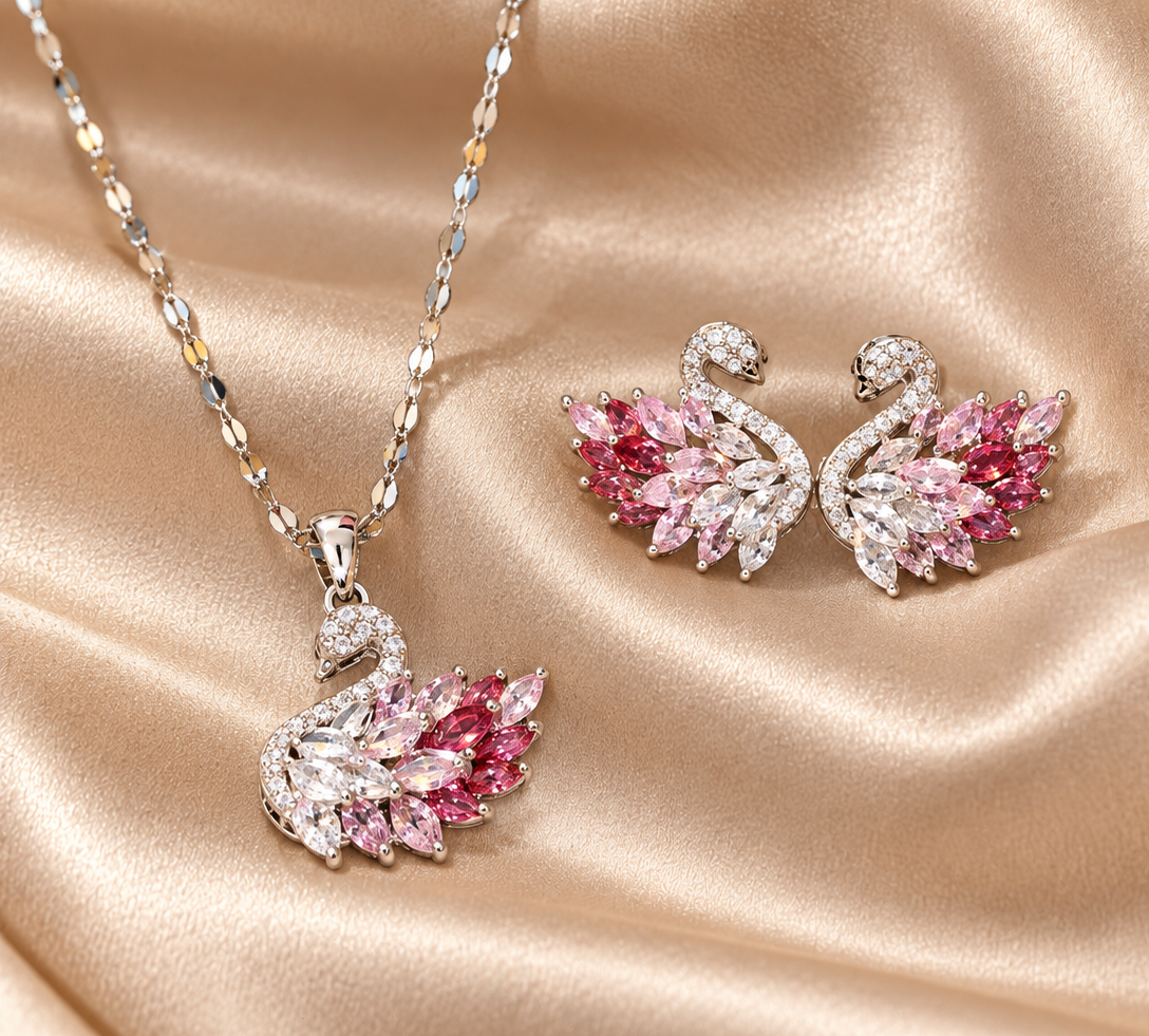 Silberfarbenes Schwan-Schmuckset mit Halskette und zwei Ohrsteckern, deren Flügel mit klaren und rosafarbenen Steinen besetzt sind, auf champagnerfarbenem Satin
