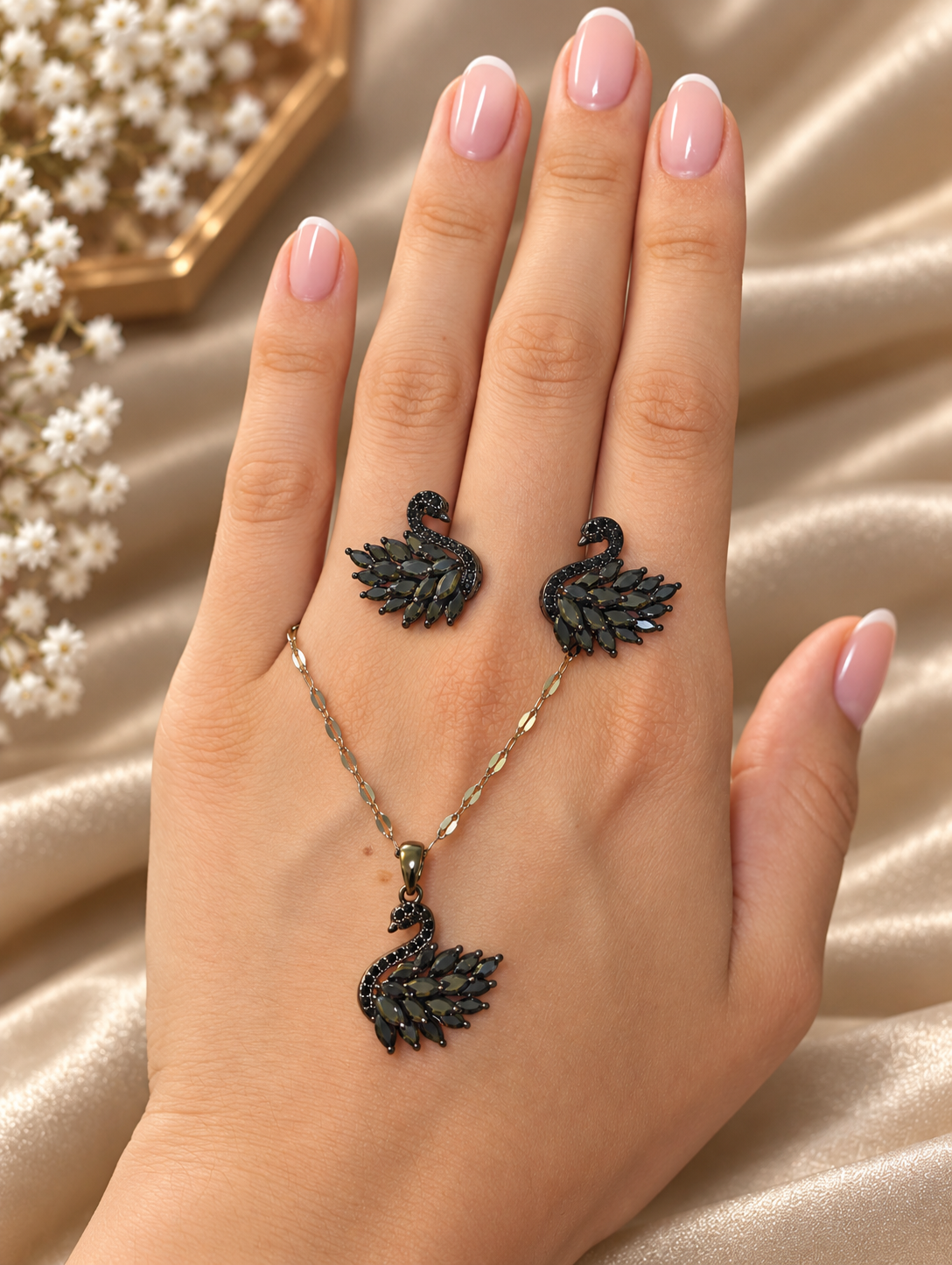 Onyx Schwan-Schmuckset auf einer Hand: zwei schwarze Schwan-Ohrstecker und silberfarbene Kette mit passendem Schwan-Anhänger
