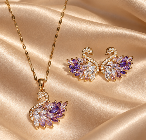 Goldfarbenes Schwan-Schmuckset mit Halskette und zwei Ohrsteckern, verziert mit klaren und fliederfarbenen Zirkonia-Steinen, auf champagnerfarbenem Satin